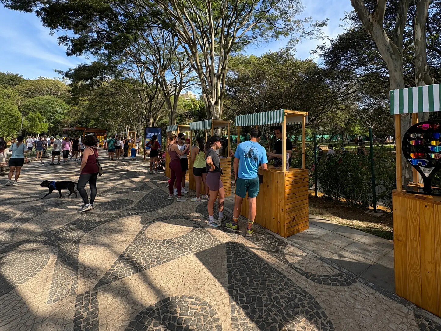Público circulando entre os estandes de madeira com toldos listrados durante a feira na Orla TotalPass